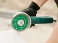 Ręka w rękawicy trzyma szlifierkę kątową z tarczą do cięcia płytek. Precyzyjne cięcie płytek ceramicznych.