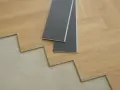 Układanie paneli winylowych w jodełkę. Dwa panele z szarym spodem leżą na drewnianej podłodze.