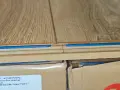 Zbliżenie na połączenie paneli podłogowych, ukazujące rodzaje zamków w panelach podłogowych i niebieską izolację.