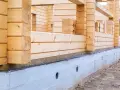 Budowa domu z bali. Widoczna izolacja drewna od betonu, chroniąca przed wilgocią.