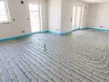 Rozłożone rury do ogrzewania podłogowego w pustym pomieszczeniu, gotowe do zalania betonem. Ciepło będzie równomiernie rozprowadzone pod przyszłymi meblami.