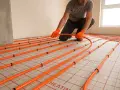 Montaż ogrzewania podłogowego pod panele winylowe. Pomarańczowe rurki układane na macie.