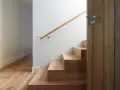 Nowoczesne schody z paneli winylowych w odcieniu drewna, z drewnianą poręczą i drzwiami.