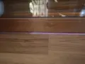 Drewniana listwa przy drzwiach balkonowych, z widoczną podłogą i fragmentem szyby.