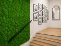 Efektowna aranżacja ściany przy schodach z żywego mchu. Obok galeria czarno-białych zdjęć w ramkach.