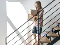 Nowa klatka schodowa w domu jednorodzinnym inspiracje: dziewczyna z kartonami schodzi po nowoczesnych schodach z drewnianymi stopniami i metalową balustradą.