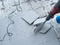 Skuwanie płytek młotem udarowym. Widać fragmenty rozbijanej podłogi i kabel zasilający.