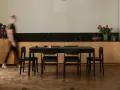 Jadalnia z czarnym stołem i krzesłami, otoczona meblami w ciepłych odcieniach dębu. W tle bukiet czerwonych róż.