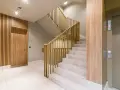 Nowoczesna klatka schodowa z drewnianą okładziną i złotymi balustradami. Osłona ściany przy schodach podkreśla elegancję wnętrza.