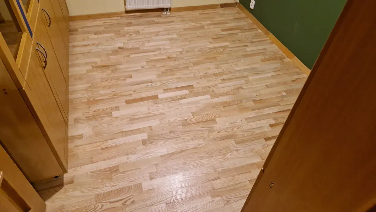 Jasny, odnowiony parkiet po cyklinowaniu lśni w słońcu. Drewniane meble dodają ciepła.