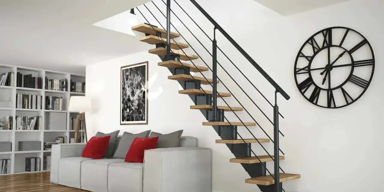 Nowoczesne schody z drewnianymi stopniami i czarną balustradą. Obok kanapa, regały z książkami i duży zegar. Wysokość balustrady zapewnia bezpieczeństwo.