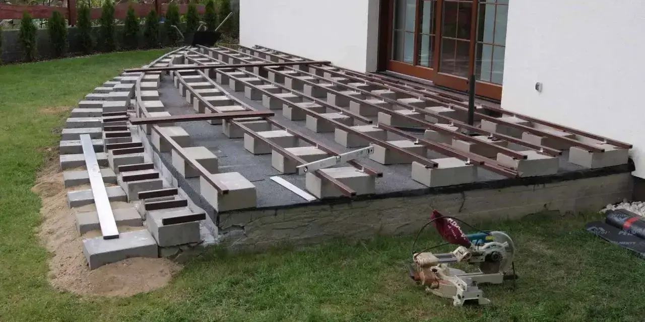 Budowa tarasu z deski kompozytowej w toku. Widać konstrukcję nośną z bloczków betonowych i legarów, gotową do ułożenia desek.