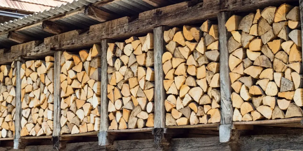 Drewno do kominka, ułożone w drewnianej szopie, czeka na suszenie desek na powietrzu.