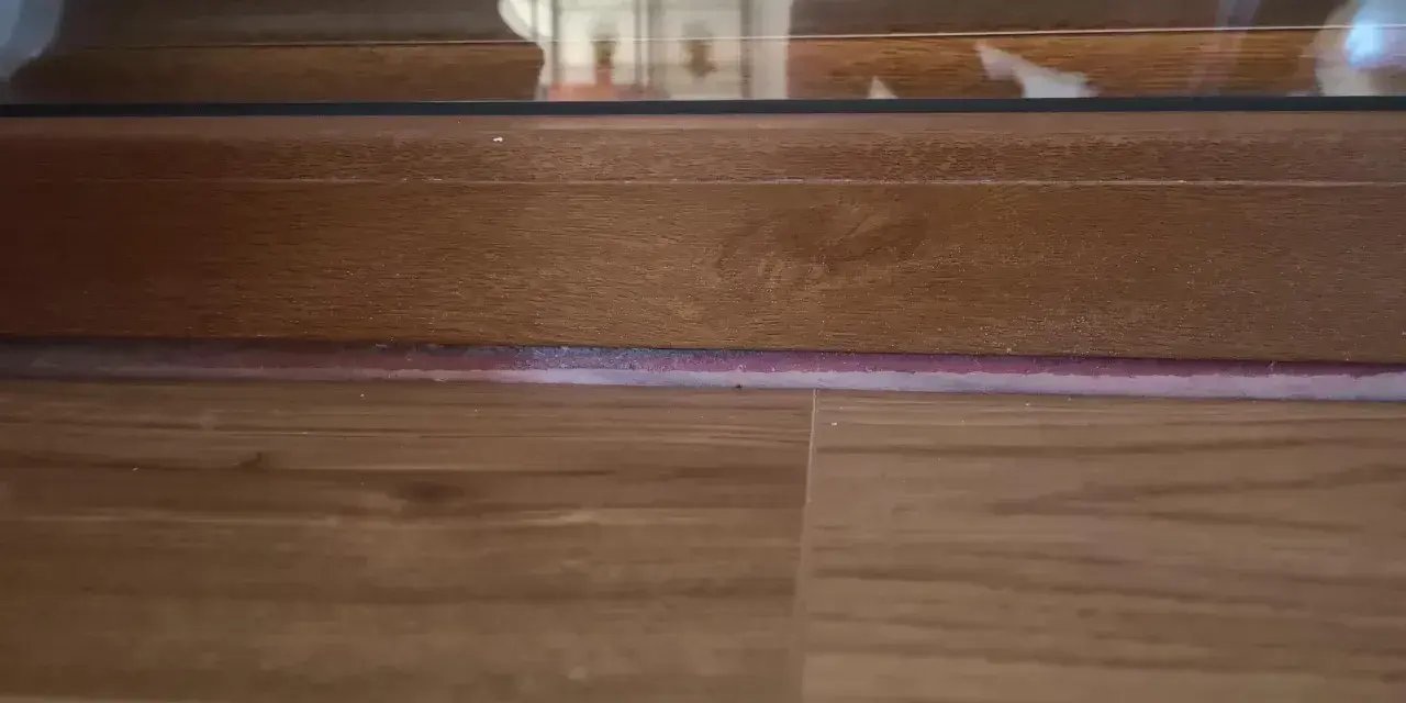 Drewniana listwa przy drzwiach balkonowych, z widoczną podłogą i fragmentem szyby.