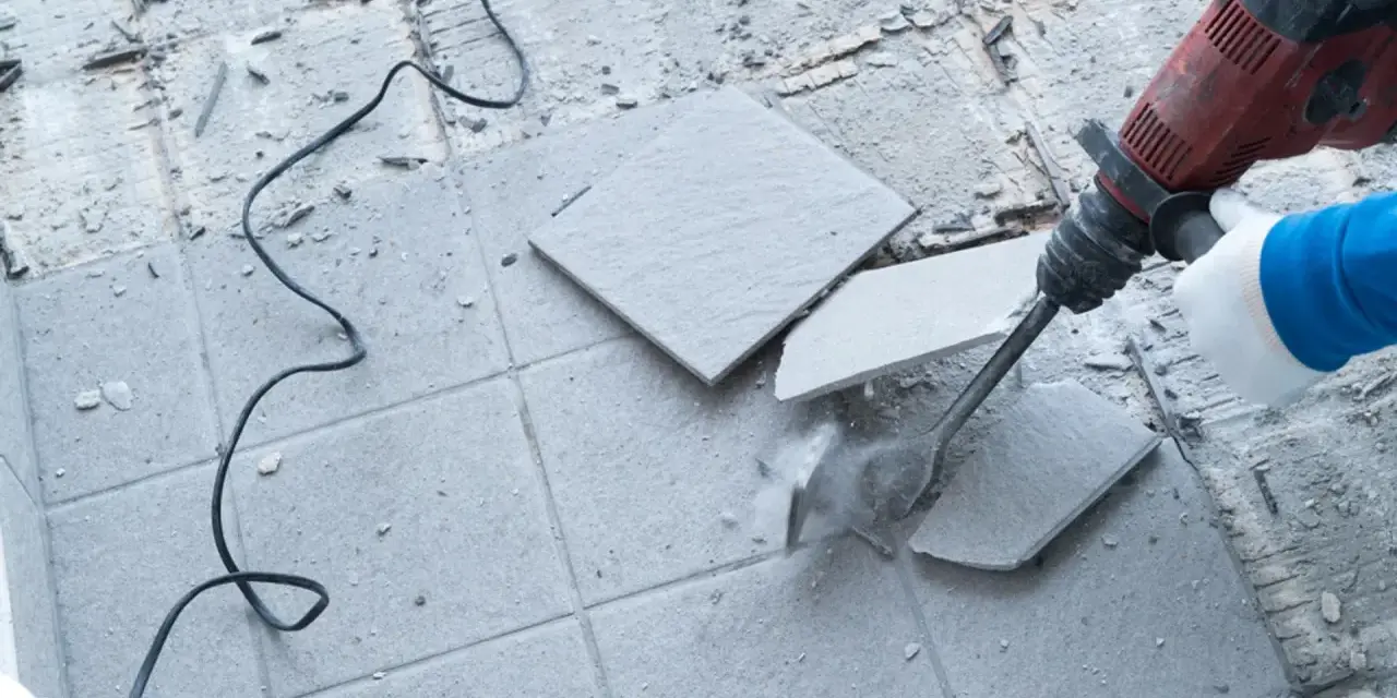 Skuwanie płytek młotem udarowym. Widać fragmenty rozbijanej podłogi i kabel zasilający.