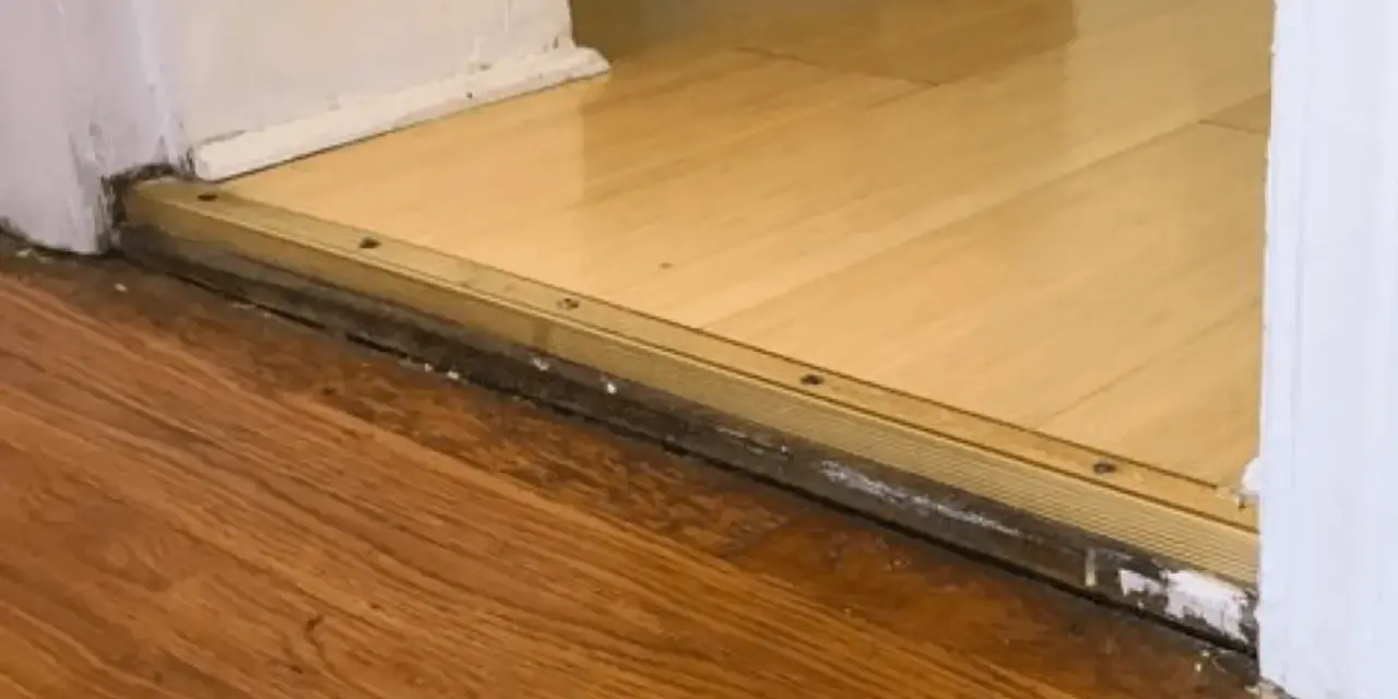 Próg z metalową listwą, widoczna różnica poziomów podłogi 4 cm między dwoma rodzajami drewna.