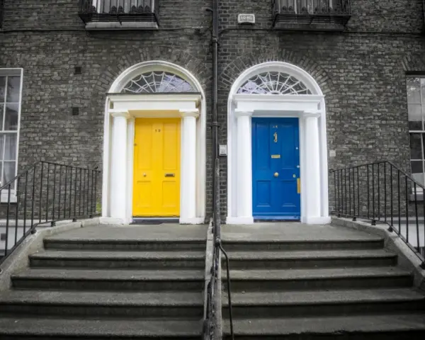 Schody zewnętrzne z czarną, metalową balustradą prowadzą do dwóch drzwi: żółtych i niebieskich.