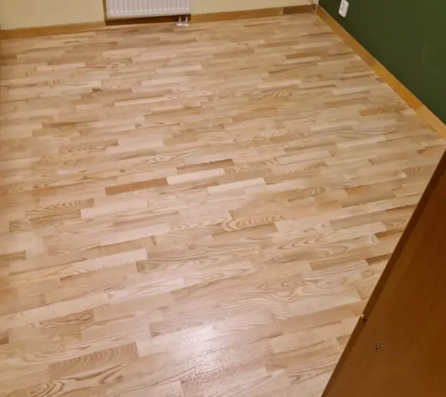 Jasny, odnowiony parkiet po cyklinowaniu lśni w słońcu. Drewniane meble dodają ciepła.