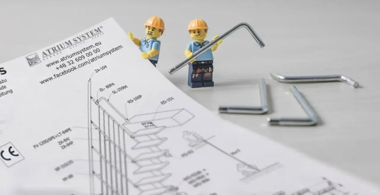 Dwaj pracownicy z klocków LEGO przygotowują się do montażu schodów modułowych, studiując instrukcję i trzymając klucze imbusowe.