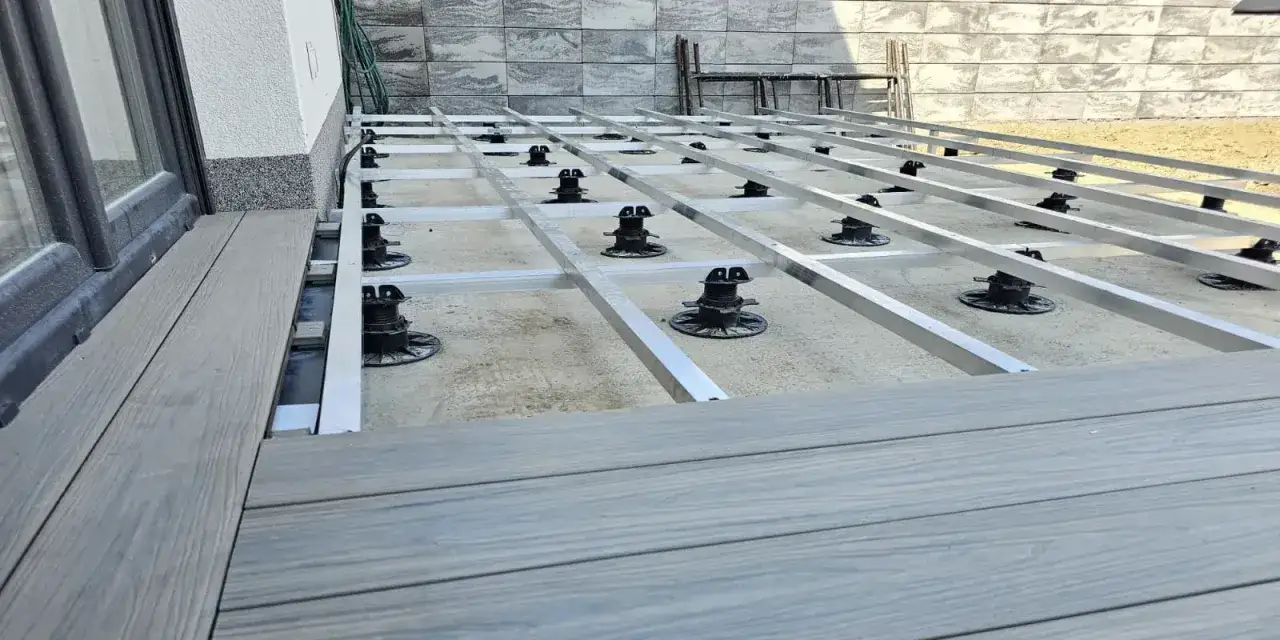 Budowa tarasu z deski kompozytowej. Widoczna konstrukcja nośna z aluminiowych profili na regulowanych podporach.
