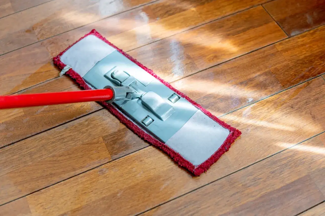 Domowe sposoby na mycie drewnianej podłogi: czerwony mop z nakładką z mikrofibry delikatnie czyści drewniany parkiet, pozostawiając lśniące deski.