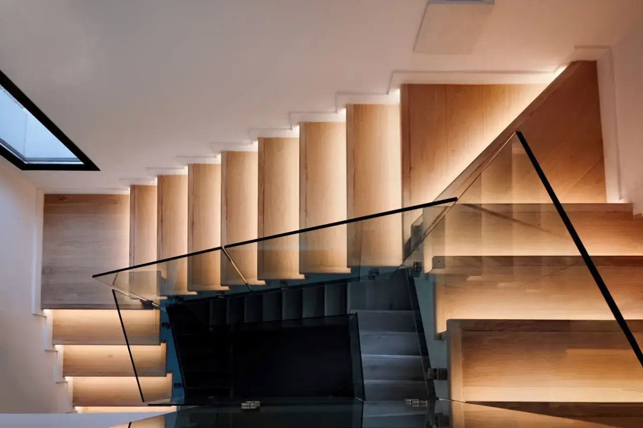 Nowoczesne schody z paneli laminowanych, oświetlone od spodu, z elegancką szklaną balustradą.