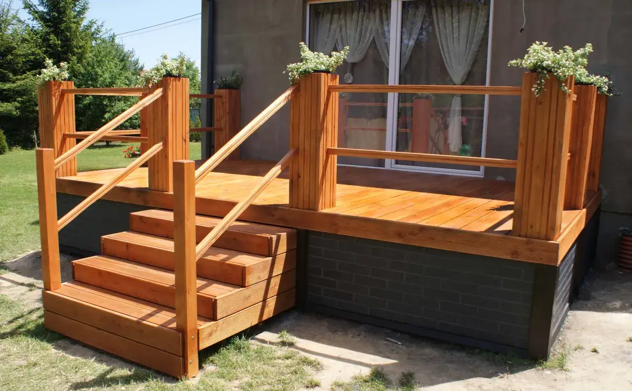 Wysoki taras ze schodami, wykonany z drewna, z balustradą i donicami z kwiatami. Idealne miejsce na relaks.