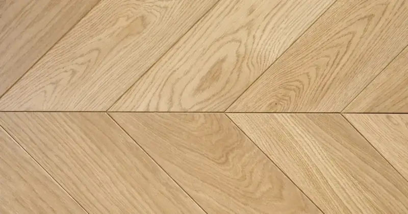 Drewniana podłoga ułożona we wzór francuska jodełka. Jasne deski tworzą elegancki, ukośny wzór.